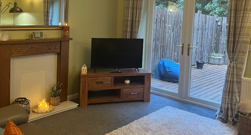 A living room with a TV, and a view to the outside decking area.